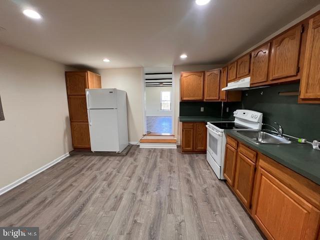 kitchen featuring a sink, dark countertops, light wood-style floors, and white appliances