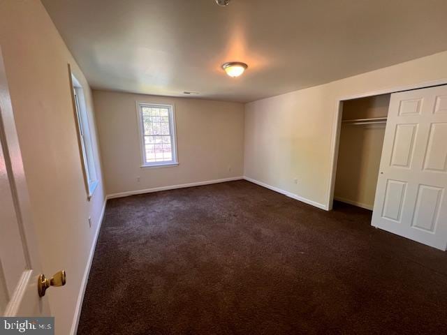 unfurnished bedroom with a closet, baseboards, and dark colored carpet