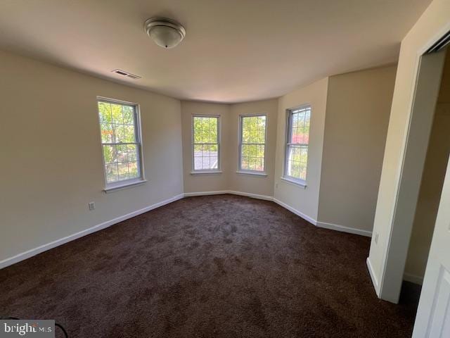 empty room with baseboards, visible vents, and dark colored carpet