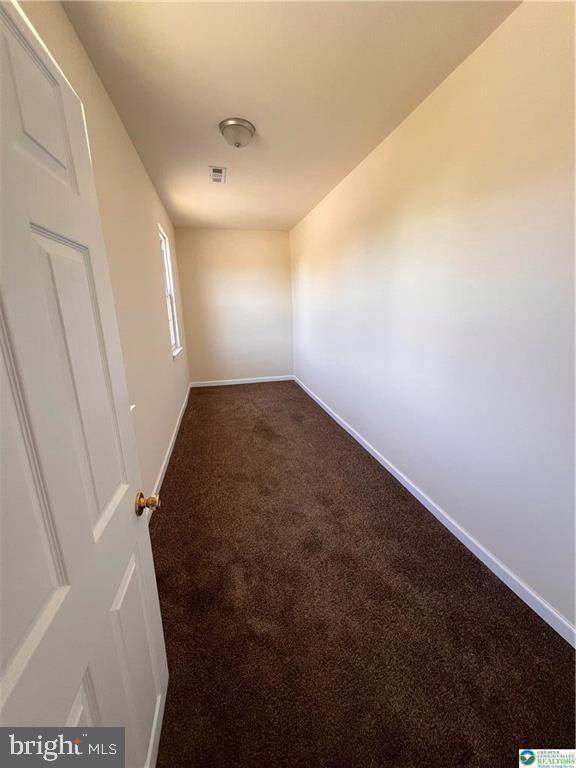 unfurnished room featuring baseboards, dark colored carpet, and visible vents