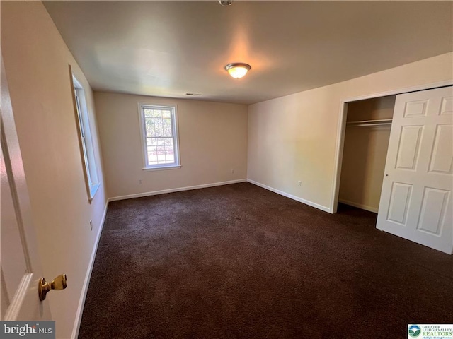 unfurnished bedroom with baseboards, dark carpet, and a closet