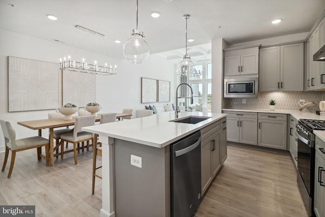 kitchen featuring a notable chandelier, a sink, stainless steel appliances, tasteful backsplash, and gray cabinetry