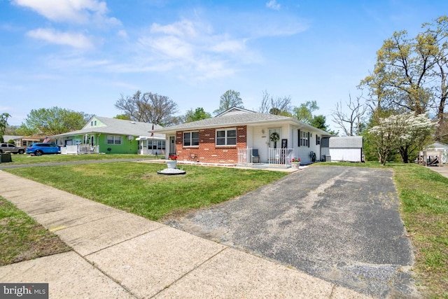 view of front of home with covered porch, a front yard, brick siding, and aphalt driveway