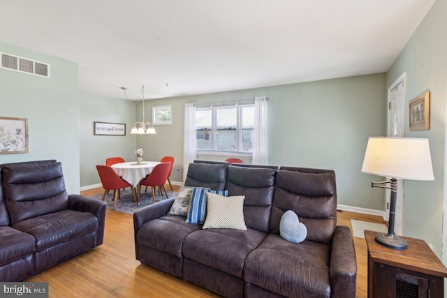 living area featuring a chandelier, baseboards, visible vents, and wood finished floors