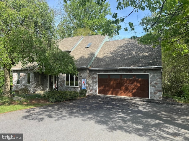 view of front facade with an attached garage, a shingled roof, driveway, and stone siding