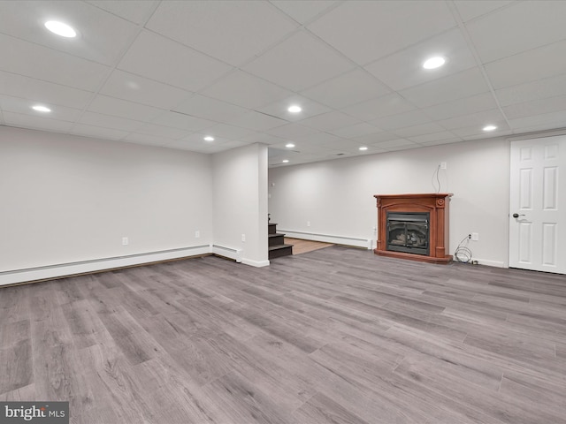 finished below grade area featuring wood finished floors, a fireplace with raised hearth, stairs, and a baseboard heating unit