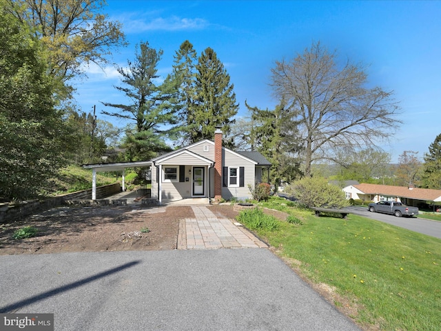 bungalow-style home with an attached carport, a chimney, and a front lawn