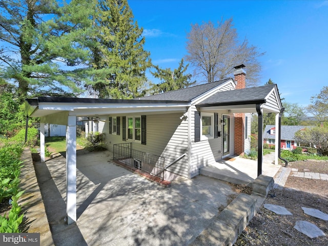 view of front of house with roof with shingles, an attached carport, a chimney, a porch, and driveway