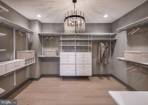 walk in closet with light wood finished floors and a notable chandelier