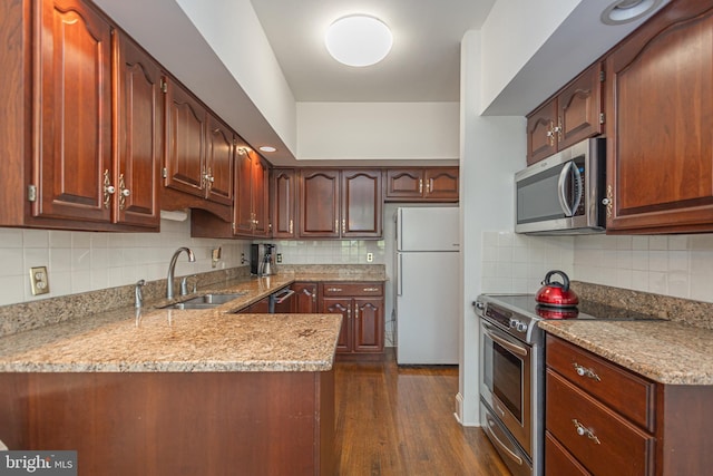 kitchen with decorative backsplash, a peninsula, dark wood-type flooring, a sink, and appliances with stainless steel finishes