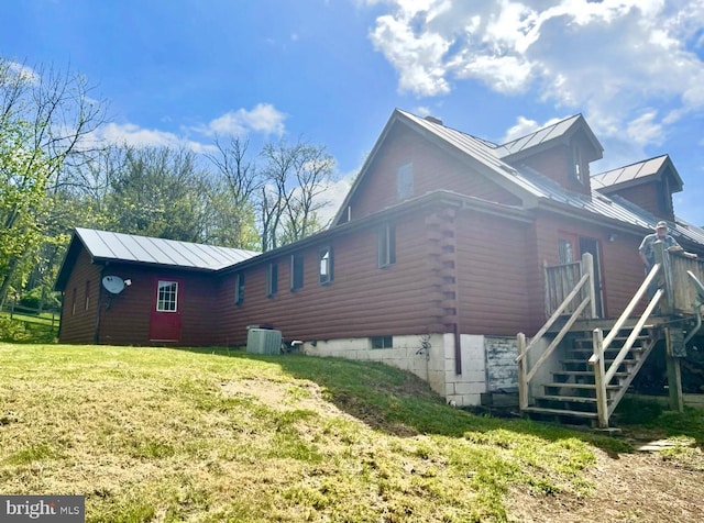 view of side of home featuring stairs, central air condition unit, a standing seam roof, a yard, and metal roof