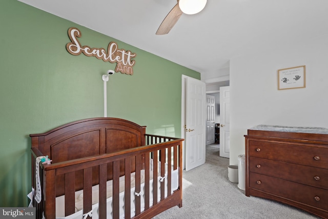 bedroom featuring light colored carpet, ceiling fan, and a nursery area