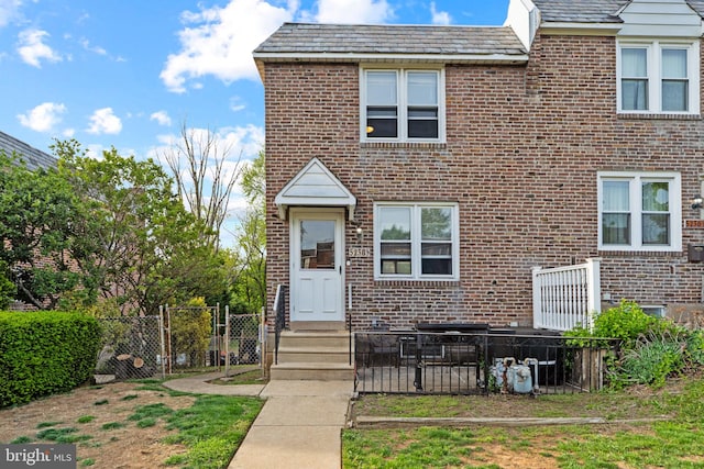 view of front facade featuring brick siding, fence, and a high end roof