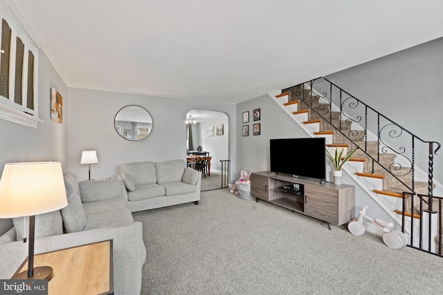 carpeted living area featuring stairway and arched walkways