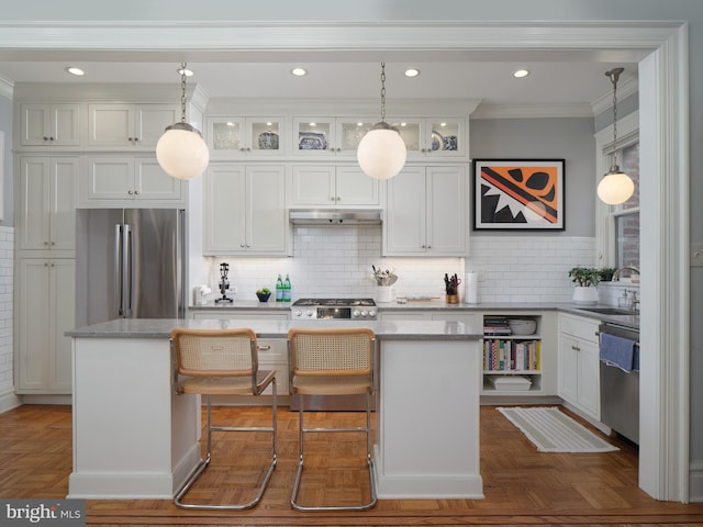 kitchen featuring a center island, a sink, under cabinet range hood, stainless steel appliances, and white cabinetry