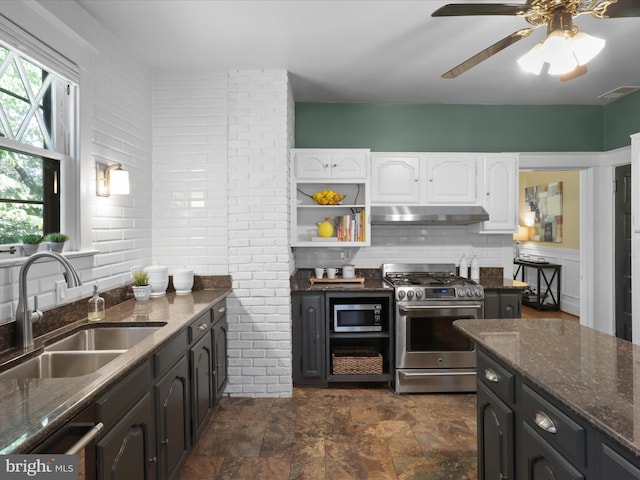 kitchen with white cabinets, appliances with stainless steel finishes, a sink, dark stone countertops, and under cabinet range hood
