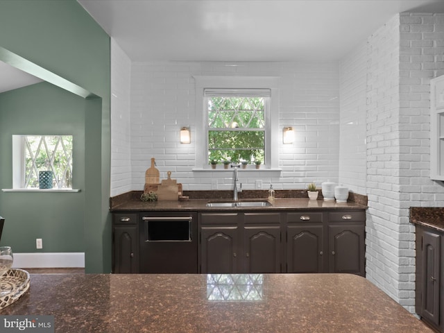 kitchen featuring dark stone counters, brick wall, a sink, and dishwasher