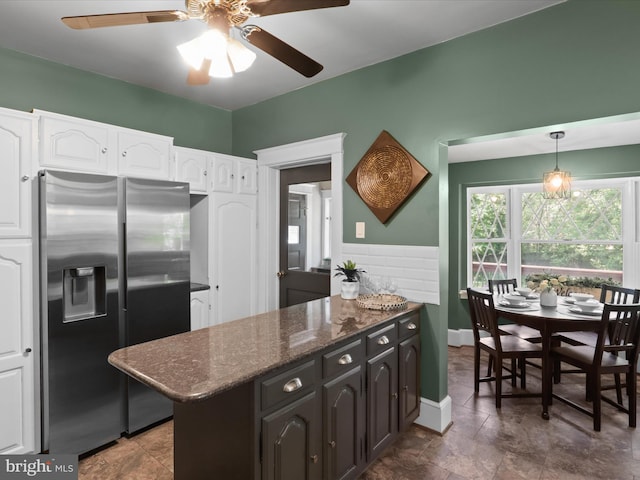 kitchen featuring white cabinets, wainscoting, stainless steel fridge with ice dispenser, dark stone countertops, and a ceiling fan