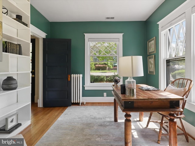 home office featuring visible vents, baseboards, radiator, and wood finished floors