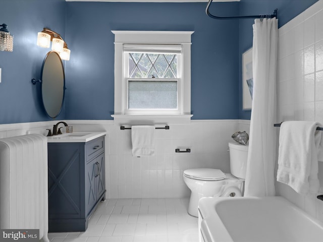 full bath featuring vanity, wainscoting, a washtub, toilet, and tile walls