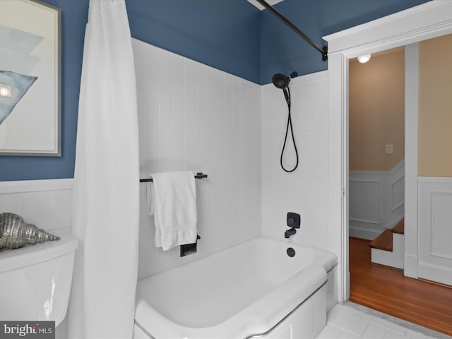 bathroom with a wainscoted wall, shower / bath combo, and toilet