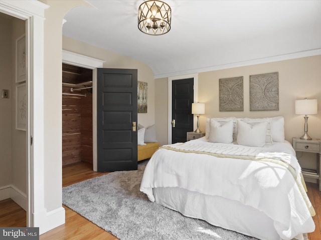 bedroom with arched walkways, baseboards, wood finished floors, and a closet