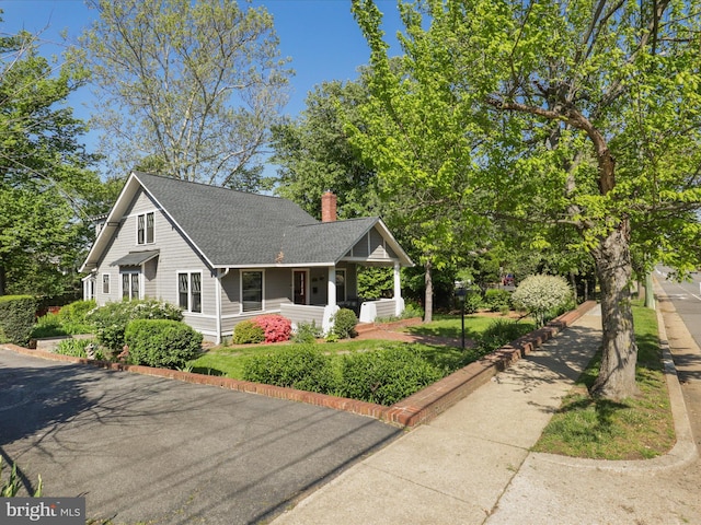 view of front of property featuring covered porch, a chimney, and roof with shingles