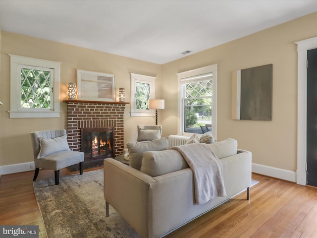 living room featuring visible vents, baseboards, a brick fireplace, and hardwood / wood-style flooring