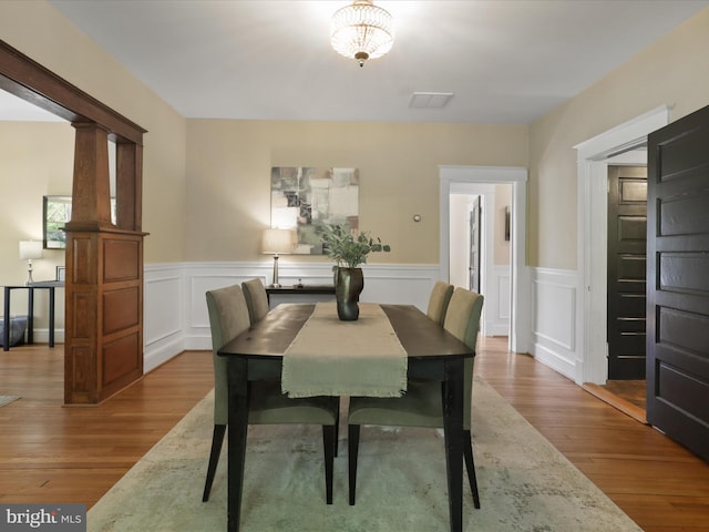 dining room featuring a decorative wall, visible vents, wood finished floors, and a wainscoted wall