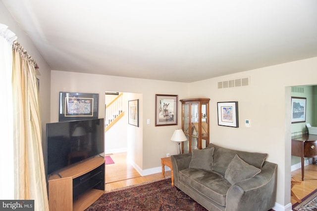 living area featuring stairs, baseboards, visible vents, and wood finished floors