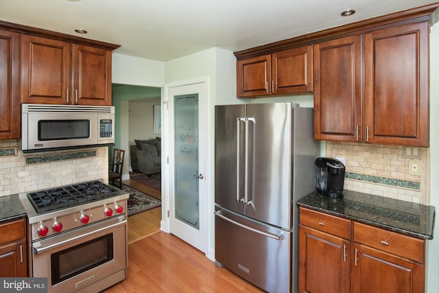 kitchen featuring high quality appliances, dark stone countertops, decorative backsplash, and light wood-type flooring