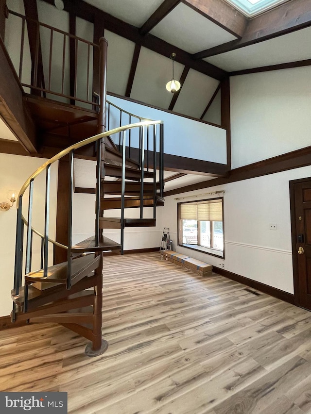 stairway with baseboards, beam ceiling, wood finished floors, and high vaulted ceiling