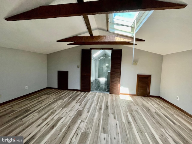 unfurnished living room featuring baseboards, visible vents, light wood finished floors, and vaulted ceiling with skylight