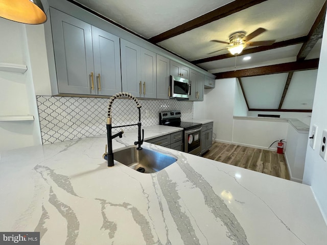 kitchen with a ceiling fan, backsplash, beam ceiling, a sink, and stainless steel appliances