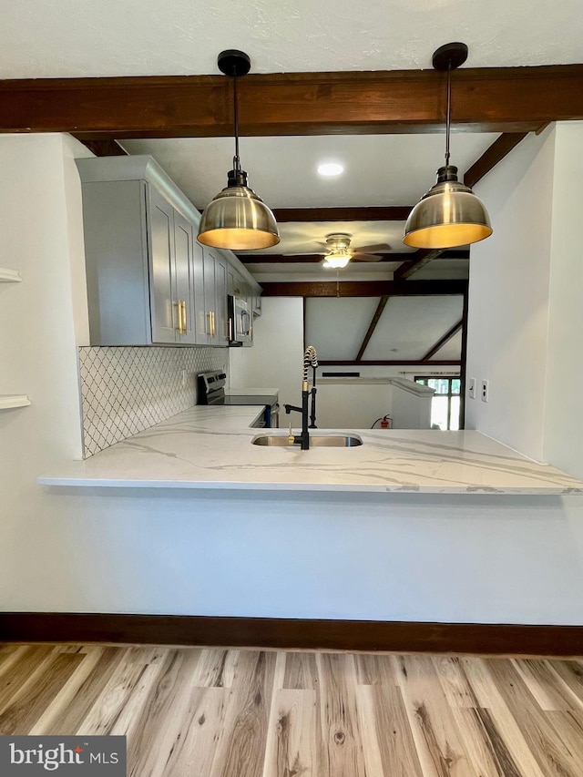 kitchen with a sink, decorative backsplash, appliances with stainless steel finishes, and beamed ceiling