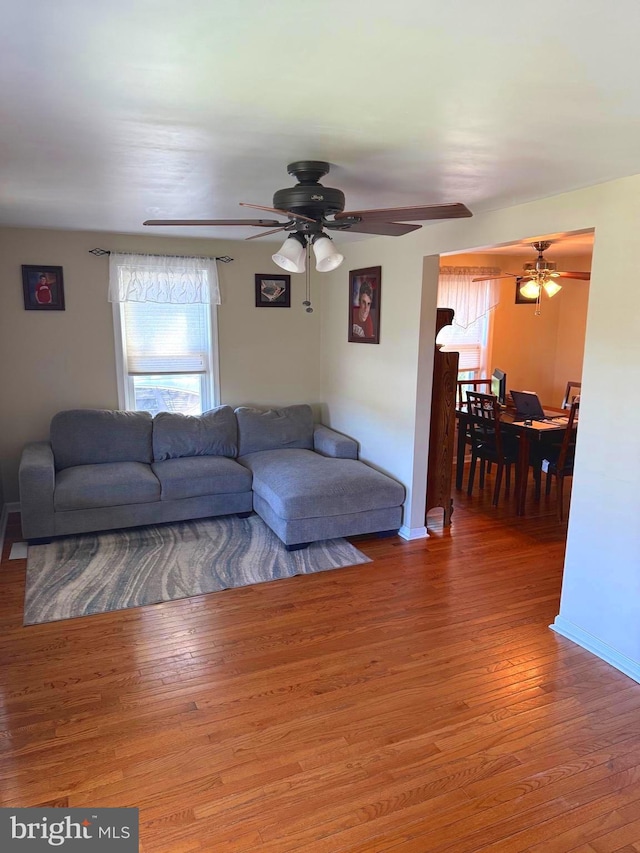 living room featuring baseboards, ceiling fan, wood finished floors, and a healthy amount of sunlight