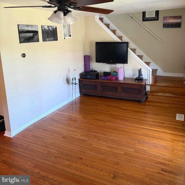 living area featuring a ceiling fan, baseboards, wood finished floors, visible vents, and stairway