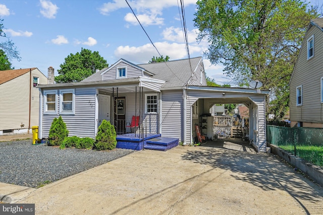 bungalow-style house with fence, a shingled roof, a porch, concrete driveway, and a carport