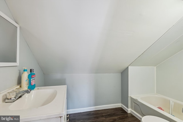 bathroom featuring vanity, lofted ceiling, wood finished floors, baseboards, and a bath