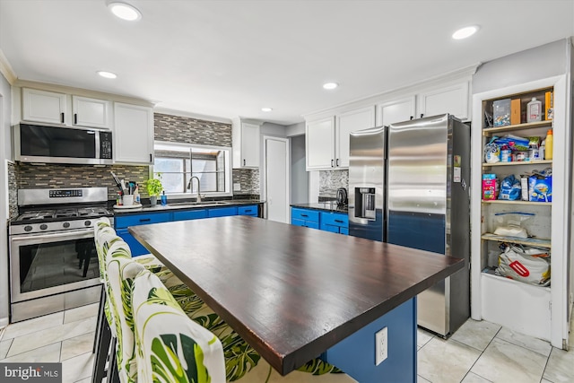 kitchen with dark countertops, tasteful backsplash, a sink, white cabinets, and stainless steel appliances