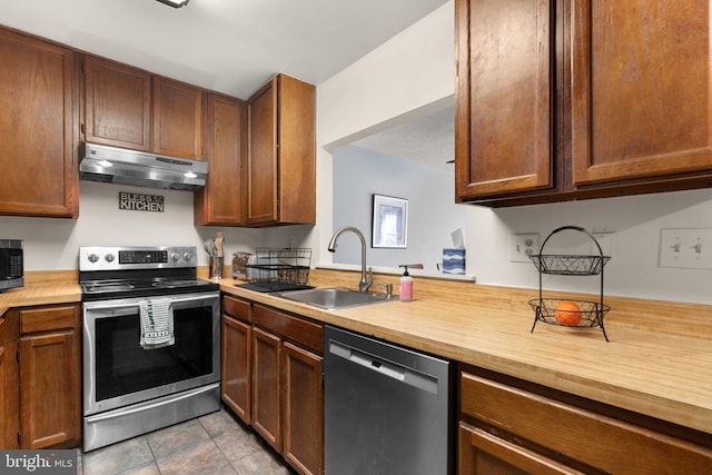 kitchen featuring appliances with stainless steel finishes, a sink, wood counters, light tile patterned floors, and under cabinet range hood