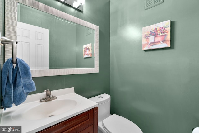 half bath featuring visible vents, toilet, and vanity