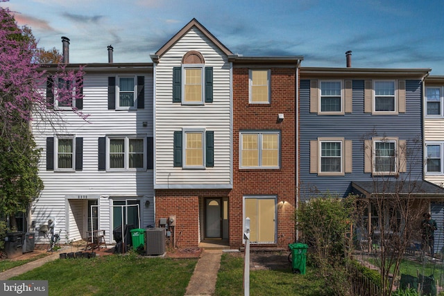 view of front facade featuring central AC, brick siding, and a front yard