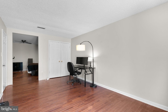 home office featuring a ceiling fan, a textured ceiling, visible vents, wood finished floors, and baseboards
