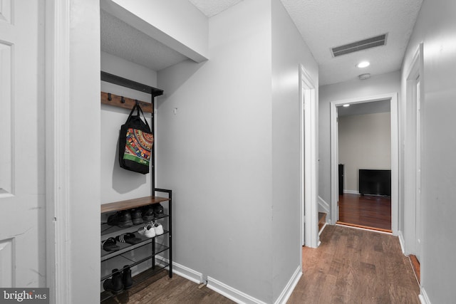 corridor with baseboards, a textured ceiling, visible vents, and wood finished floors