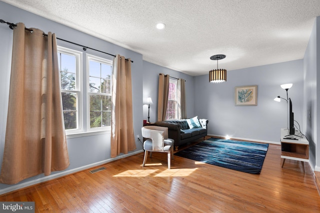 living area featuring a textured ceiling, visible vents, baseboards, and hardwood / wood-style flooring