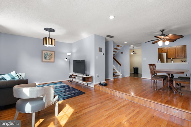living area featuring stairs, a ceiling fan, a textured ceiling, and wood finished floors