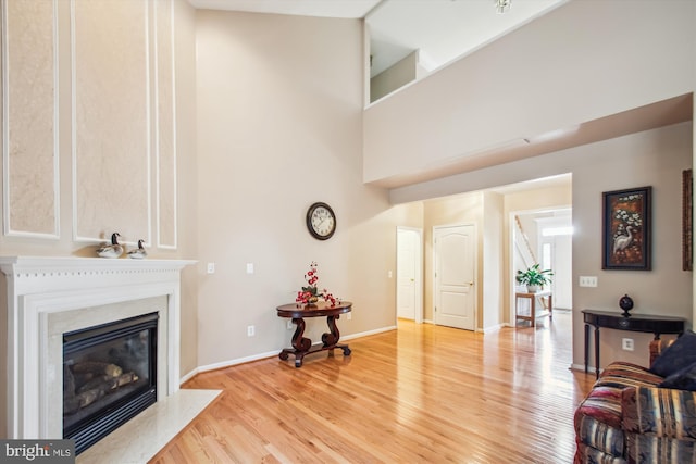 living room featuring a high ceiling, baseboards, light wood finished floors, and a high end fireplace