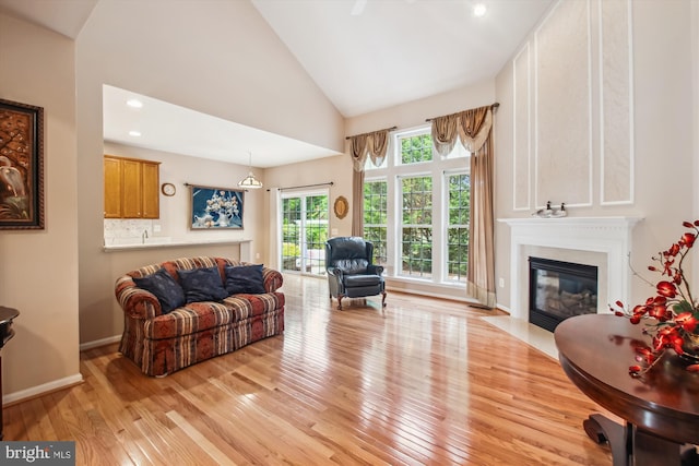 living room with a fireplace with flush hearth, light wood-type flooring, high vaulted ceiling, baseboards, and recessed lighting