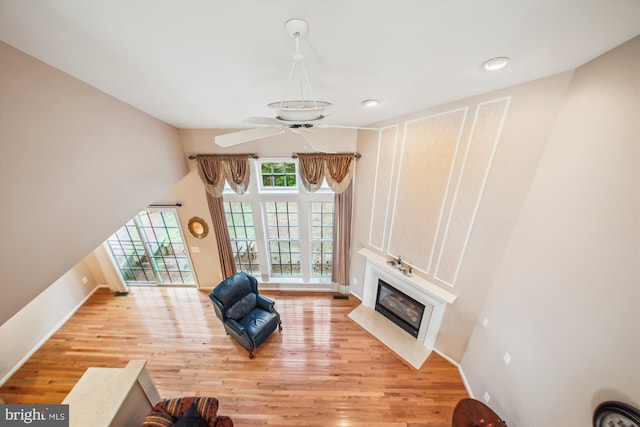 living room with a ceiling fan, baseboards, a fireplace with flush hearth, and light wood-type flooring